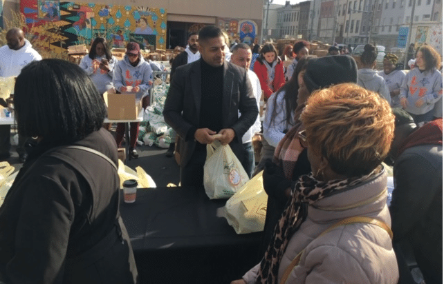 The image shows lawyer Sameer Chopra participating in a turkey giveaway service in Brooklyn.