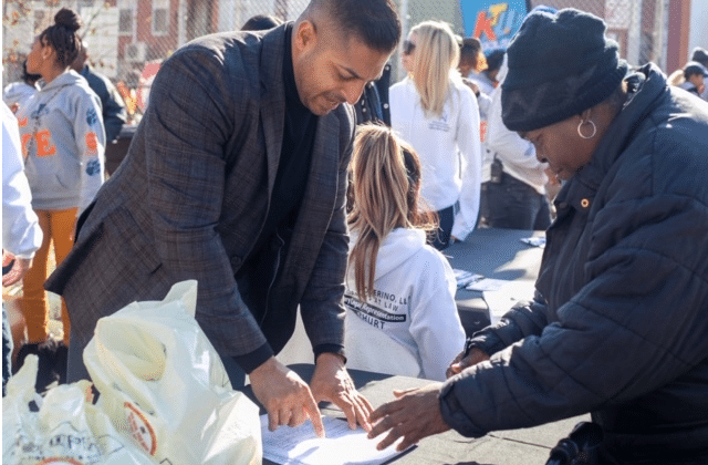 The image shows attorney Sameer Chopra actively engaged in a turkey giveaway service in Brooklyn.