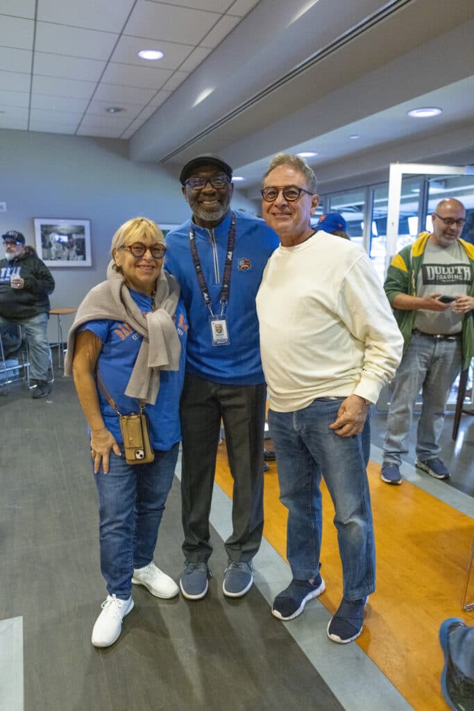 Trio of team members of Chopra & Nocerino smiling at New York Mets game from wider angle