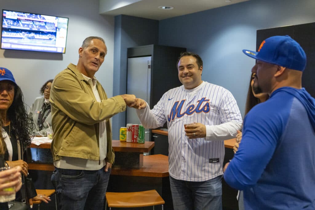 Alex Nocerino fist bumping team member while smiling at New York Mets game