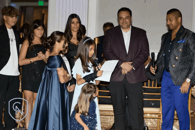 Alex Nocerino and Sameer Chopra's family standing at the gala while Sameer's daughter give a speech
