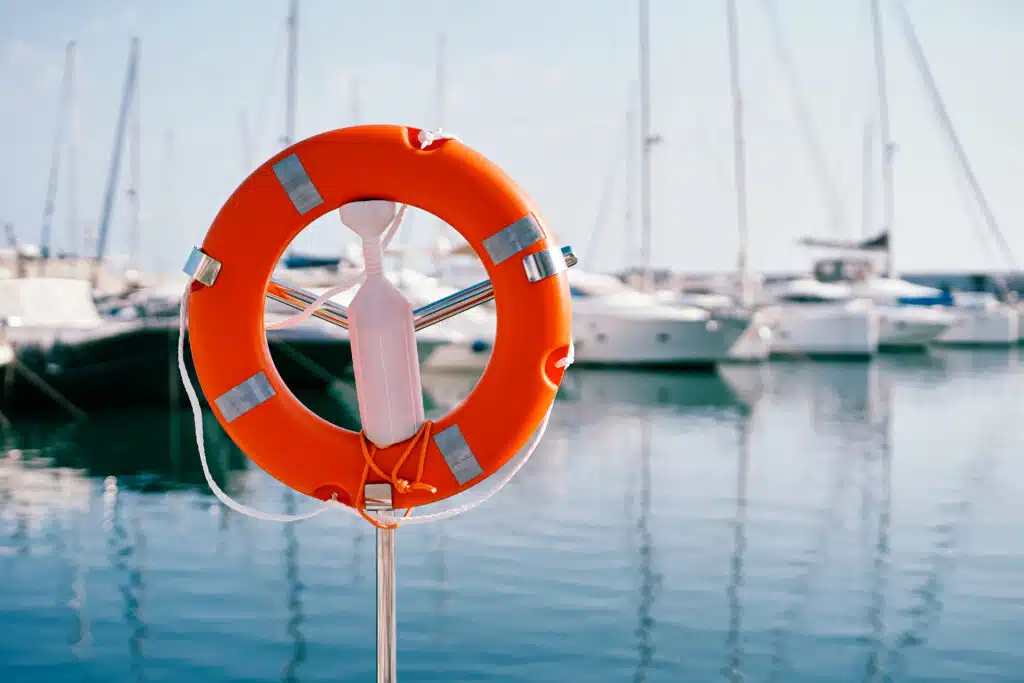 Red lifebuoy on a metal stand with white plastic fastener by the sea