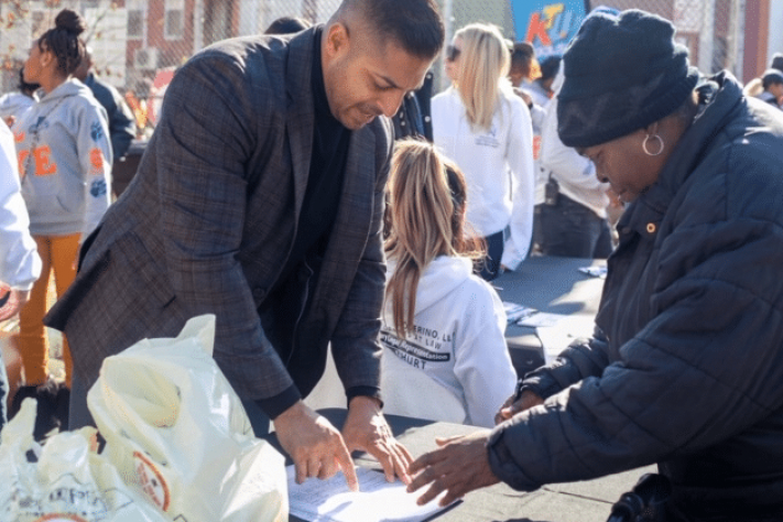 Sameer Chopra talking to a woman and reviewing a list at a turkey giveaway sponsored by Chopra & Nocerino
