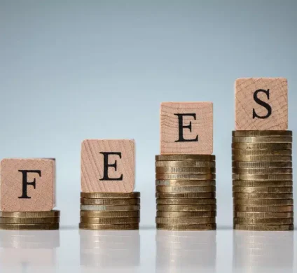 "Fees" spelled out in wooden blocks on top of stacks of coin