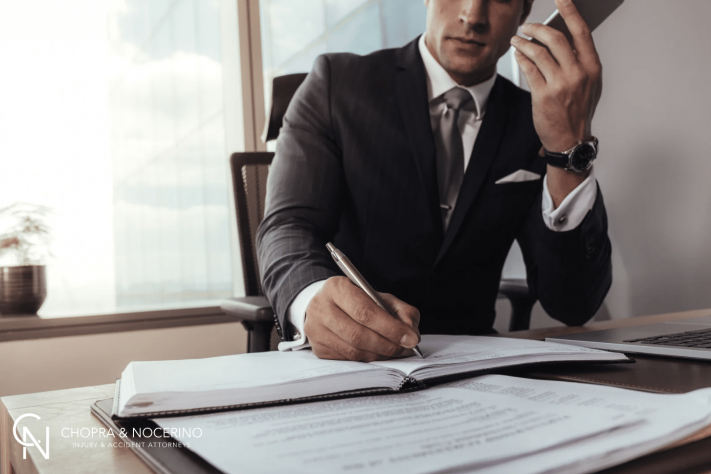 A lawyer sitting at their desk writing notes while on the phone with their client