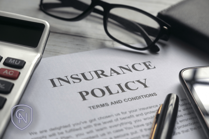 insurance policy paperwork on a desk next to glasses, a pen, a calculator and a wallet